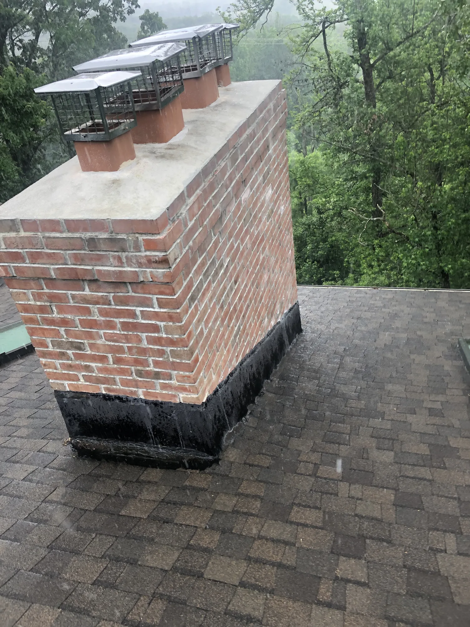 Brick chimney rising above roof shingles with capped flues