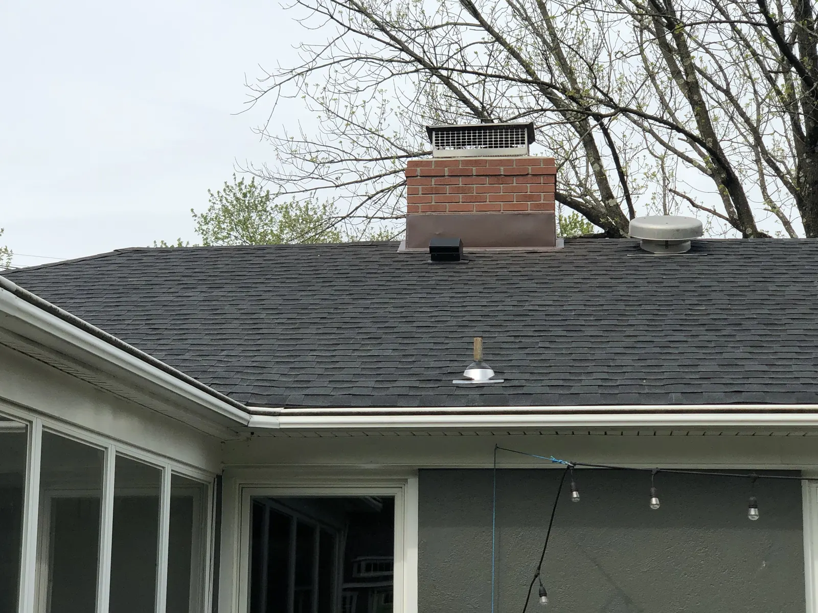 Gray asphalt shingle roof with a brick chimney and roof vents